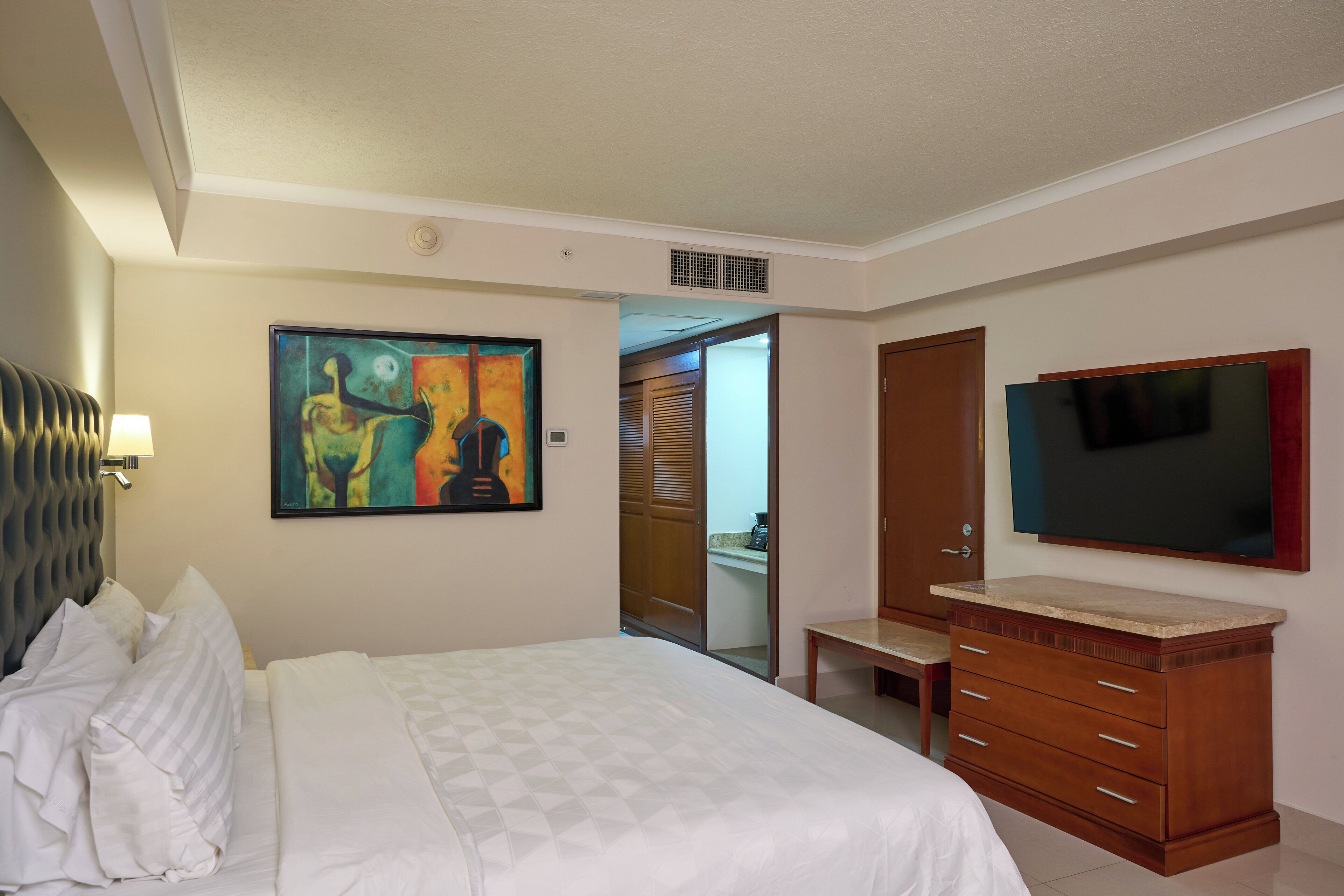 A hotel room with a bed, a painting, a TV, and a wooden cabinet.