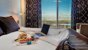 Quarto de hotel com cama, laptop, itens de café da manhã e vista para a cidade.
