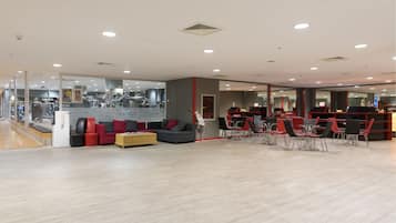 Un gimnasio moderno con equipamiento cardiovascular, una zona de recepción y un área de descanso con sillas rojas y un sofá gris.