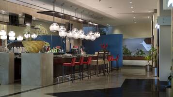 A modern restaurant with a central bar, red chairs, hanging spherical lights, and a blue accent wall.