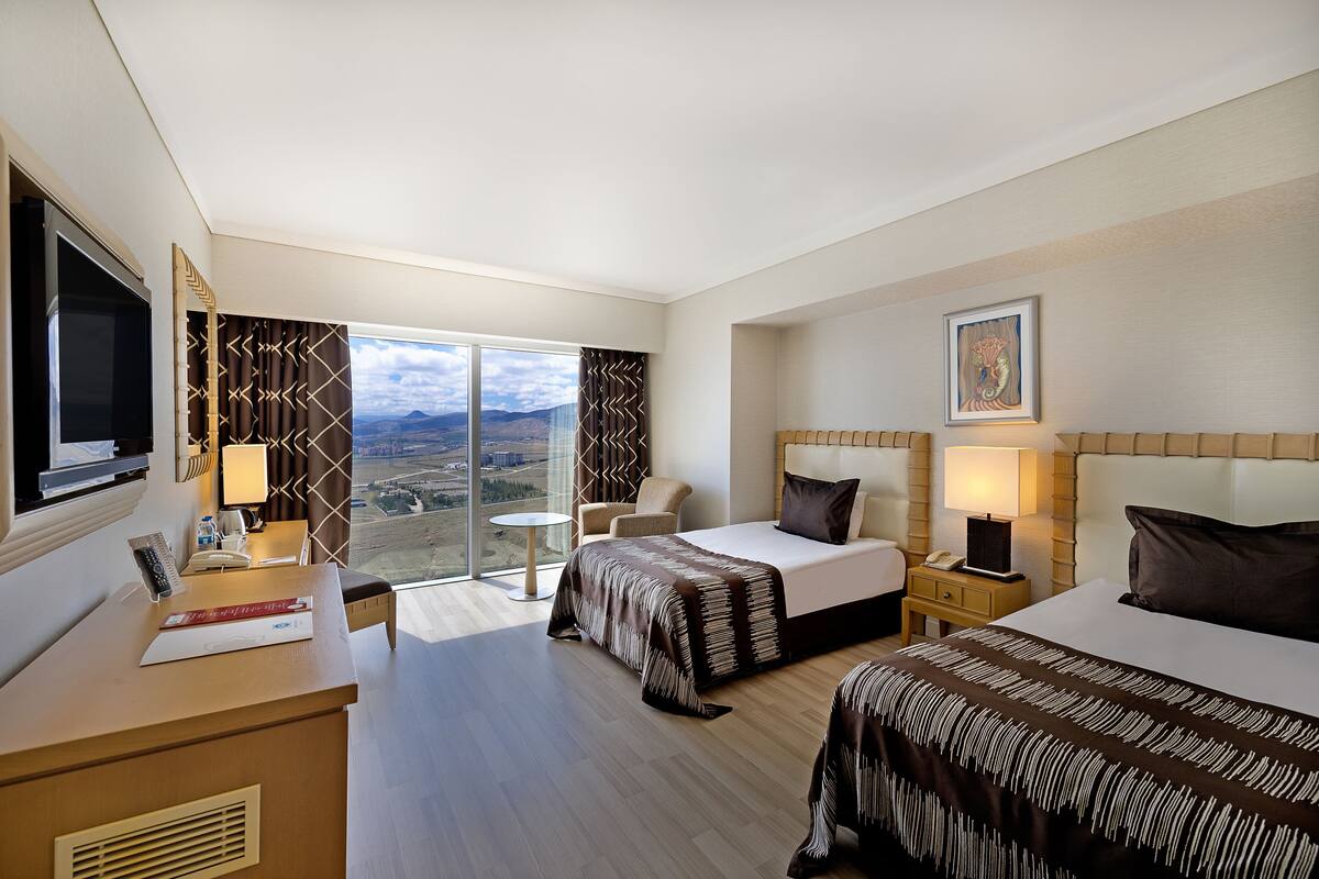 Ein Hotelzimmer mit Bett, Schreibtisch, Sessel, Nachttisch, Fernseher und einem großen Fenster mit Aussicht.