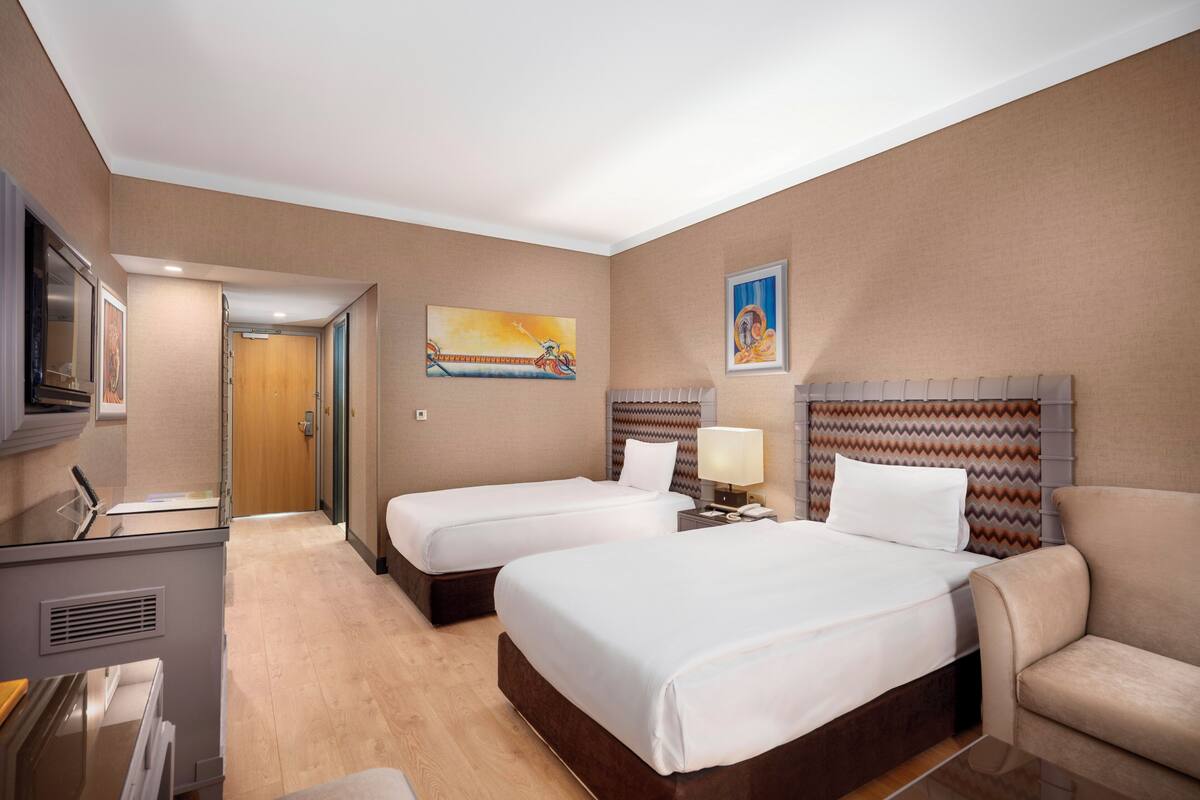 Ein Hotelzimmer mit zwei Betten, einem Fernseher, einem Schreibtisch und einem Sessel.