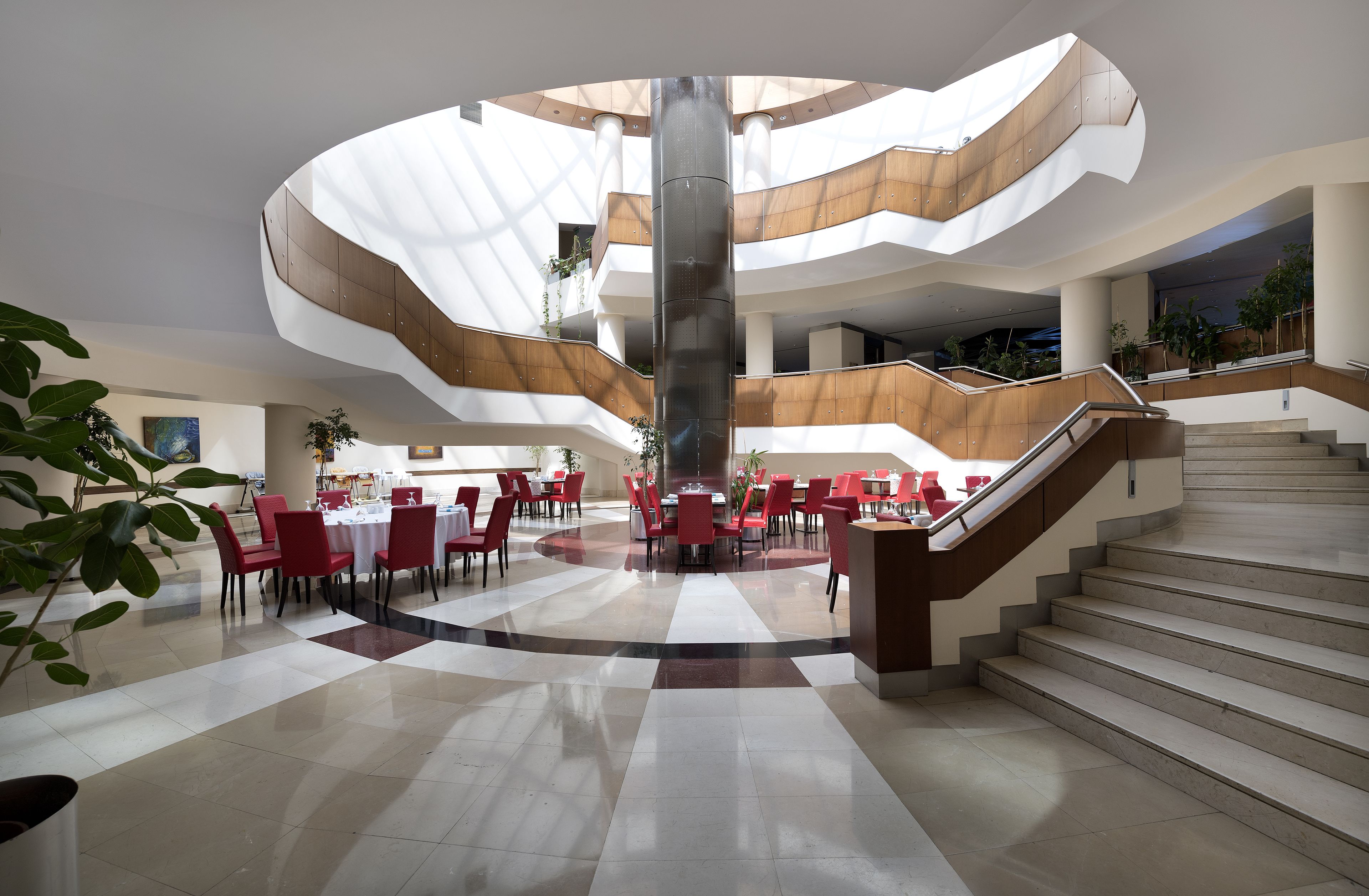 Ein geräumiger Innenhof mit einer zentralen Treppe, mehreren Essbereichen und einer hohen Decke mit Tageslicht.