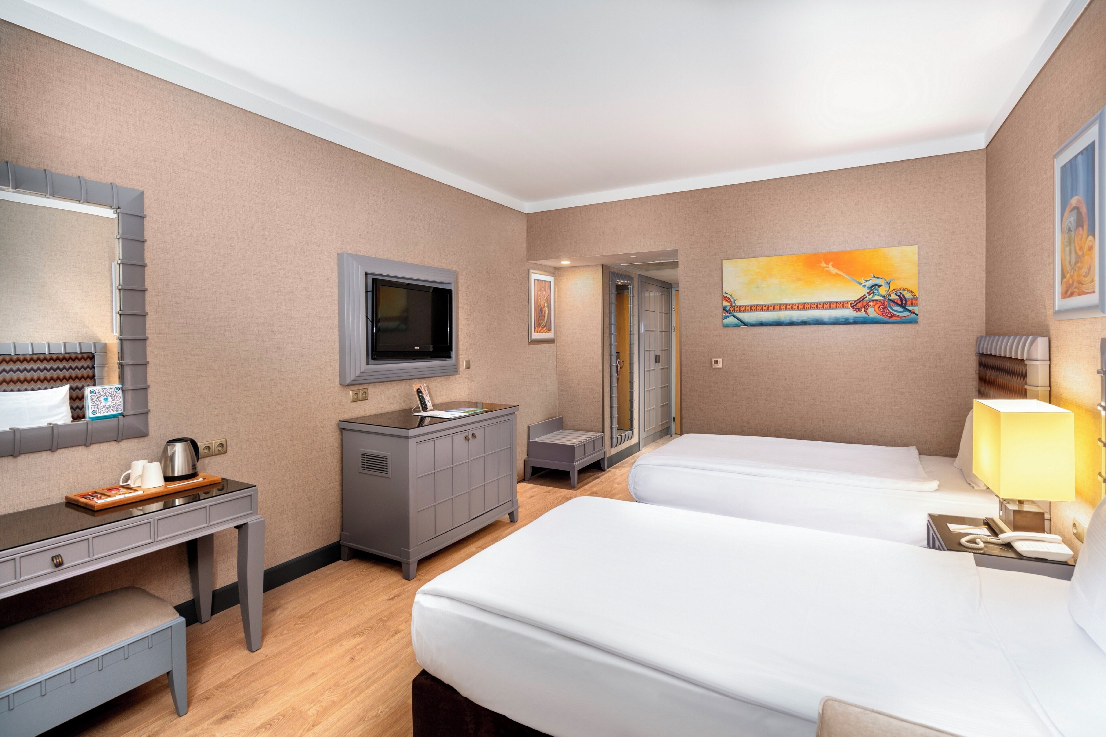 A hotel room with two beds, a desk with a coffee maker, a TV, and artwork on the walls.