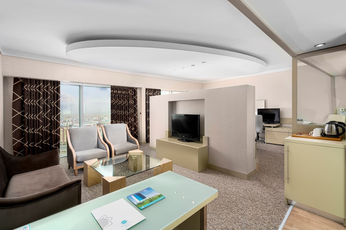 Ein modernes Hotelzimmer mit einer Sitzecke, einem Flachbildfernseher, einem Schreibtisch mit Computer und einer Küchenzeile.
