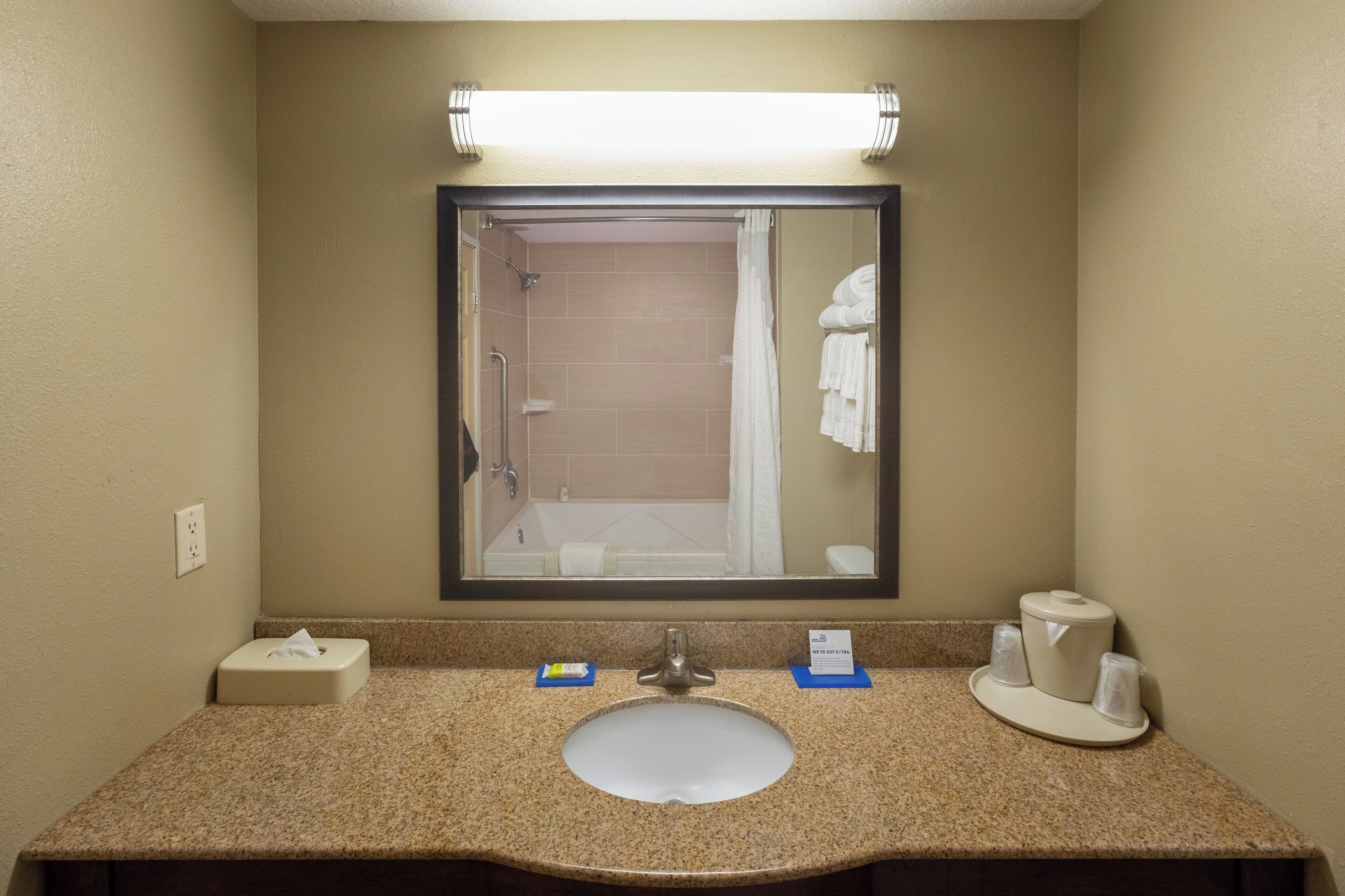 A hotel bathroom with a sink, mirror, towel rack, and a hand dryer.
