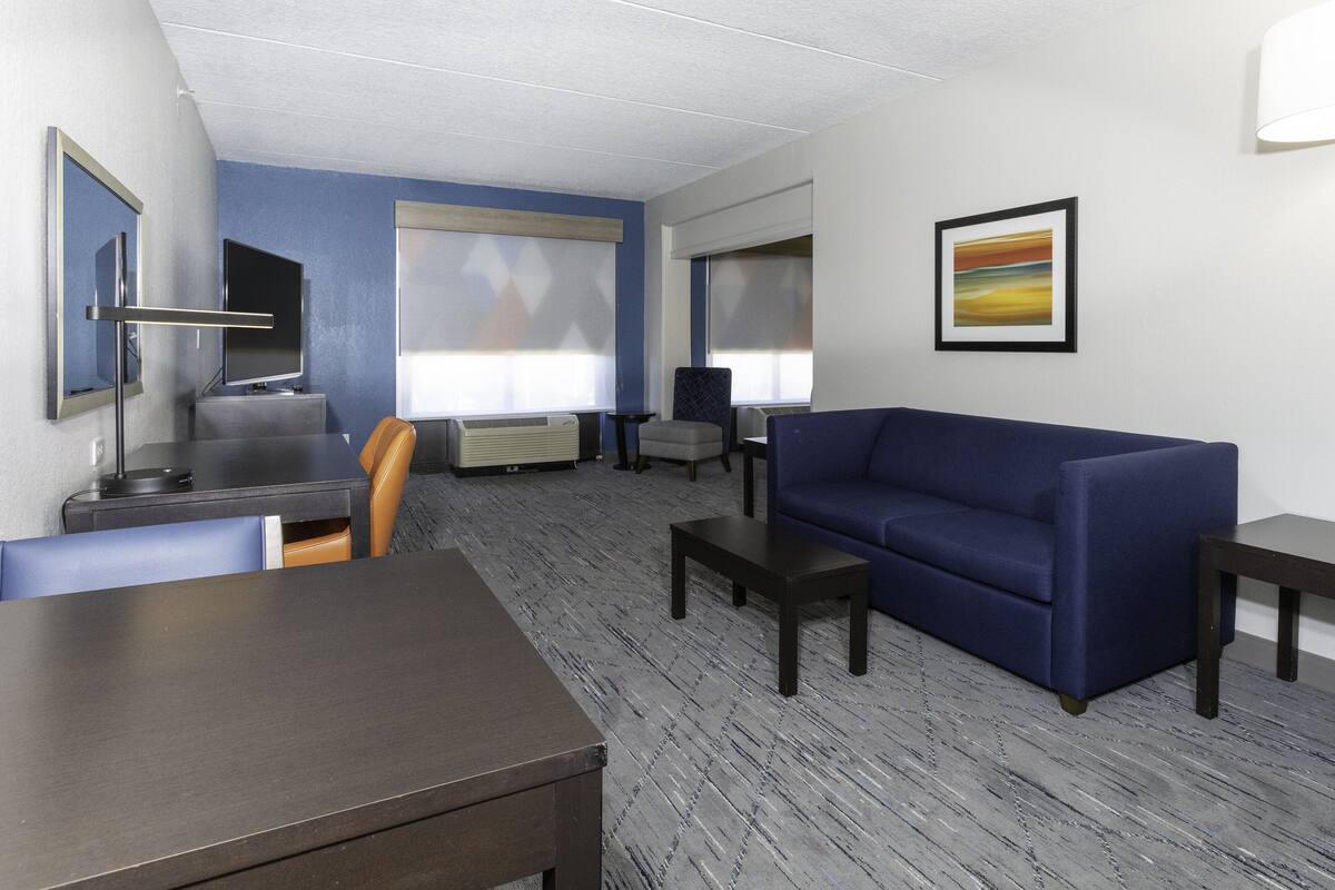 Une chambre d’hôtel avec un canapé bleu, une table à manger, un téléviseur et un tableau au mur.