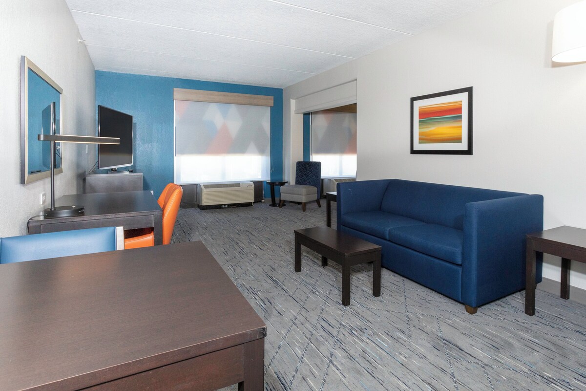 Ein Hotelzimmer mit einem blauen Sofa, einem Esstisch, einem Fernseher und einem Bild an der Wand.