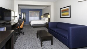 Ein Hotelzimmer mit einem Bett, einem Schreibtisch, einem Sessel, einer Couch und einem Fernseher.