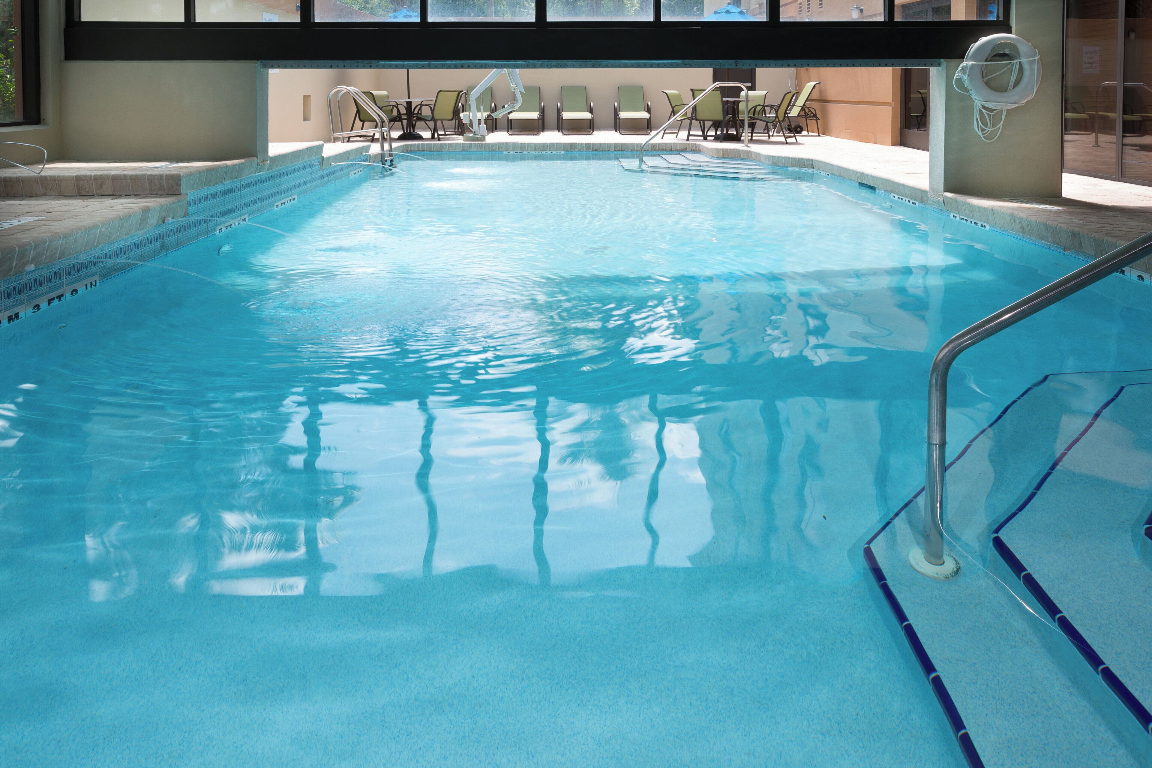 Una piscina con tabla de clavados y sillas de descanso.