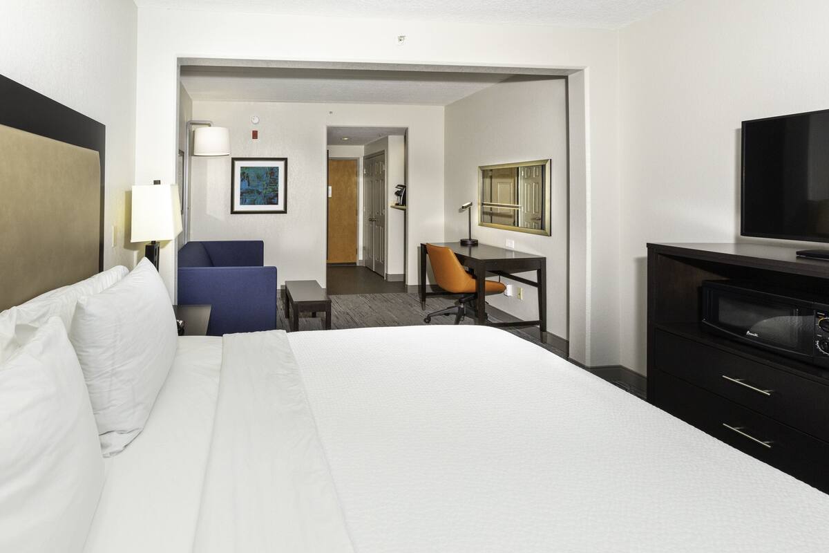 Une chambre d’hôtel avec un grand lit, un bureau avec une chaise, une télévision et une porte donnant sur une autre pièce.