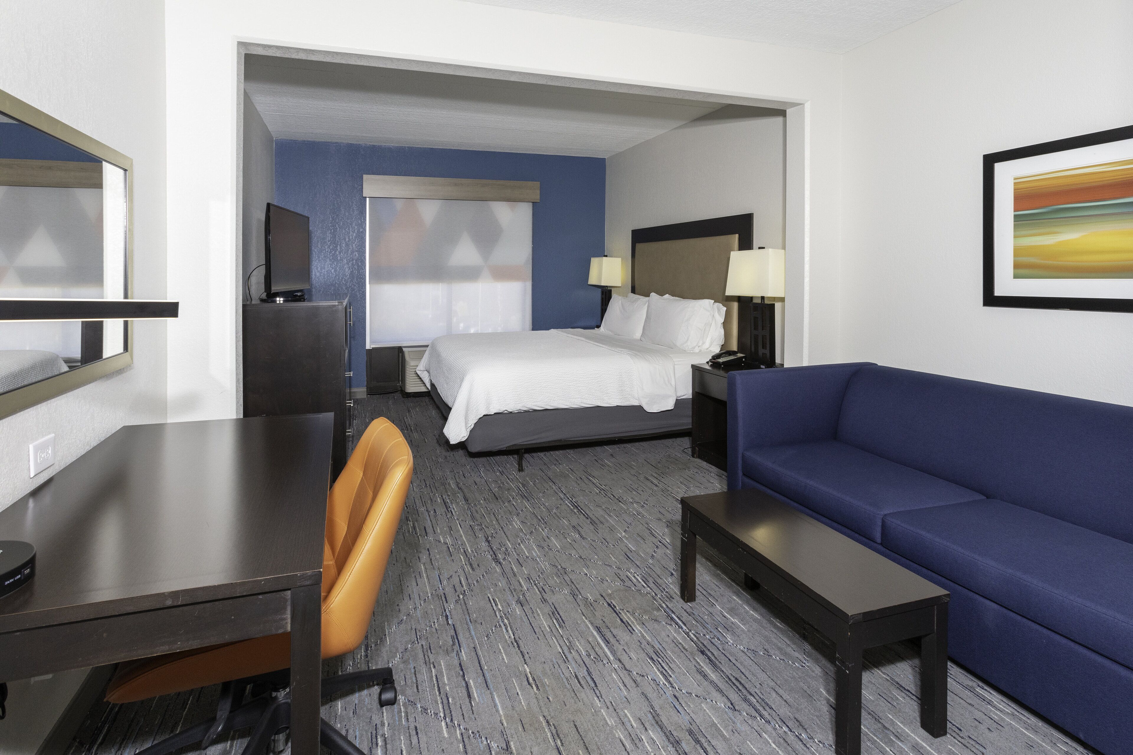 A hotel room with a bed, a desk, a chair, a sofa, and a TV.