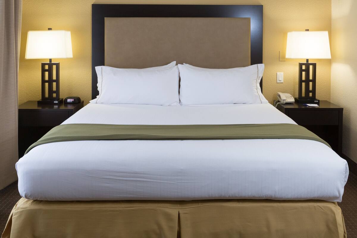 Une chambre d’hôtel avec un grand lit, deux tables de chevet avec des lampes, un téléphone et une tête de lit marron.