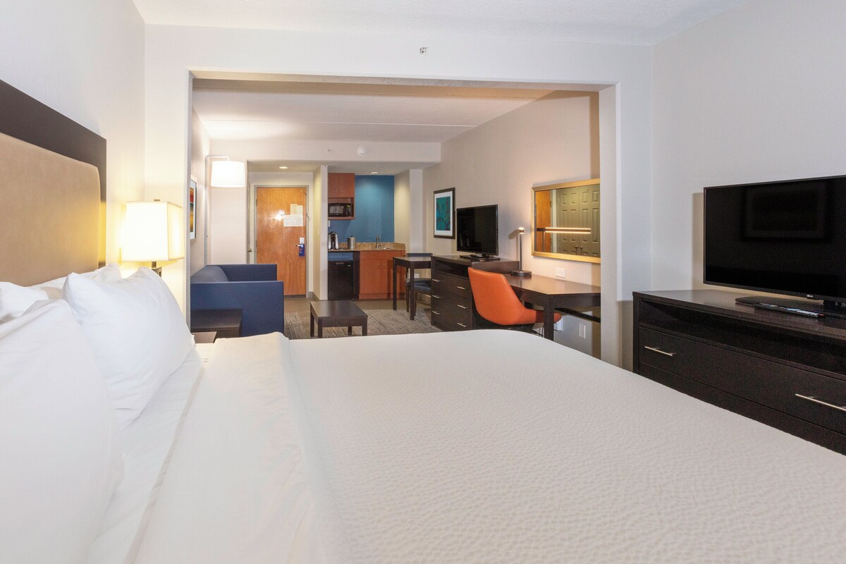 Ein Hotelzimmer mit einem großen Bett, einem Schreibtisch, einem Fernseher und einer Küchenzeile.