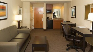 Ein Hotelzimmer mit Sofa, kleinem Tisch, Schreibtisch mit Stuhl, Mikrowelle, Kaffeemaschine und Spüle.