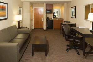 Ein Hotelzimmer mit Sofa, kleinem Tisch, Schreibtisch mit Stuhl, Mikrowelle, Kaffeemaschine und Spüle.