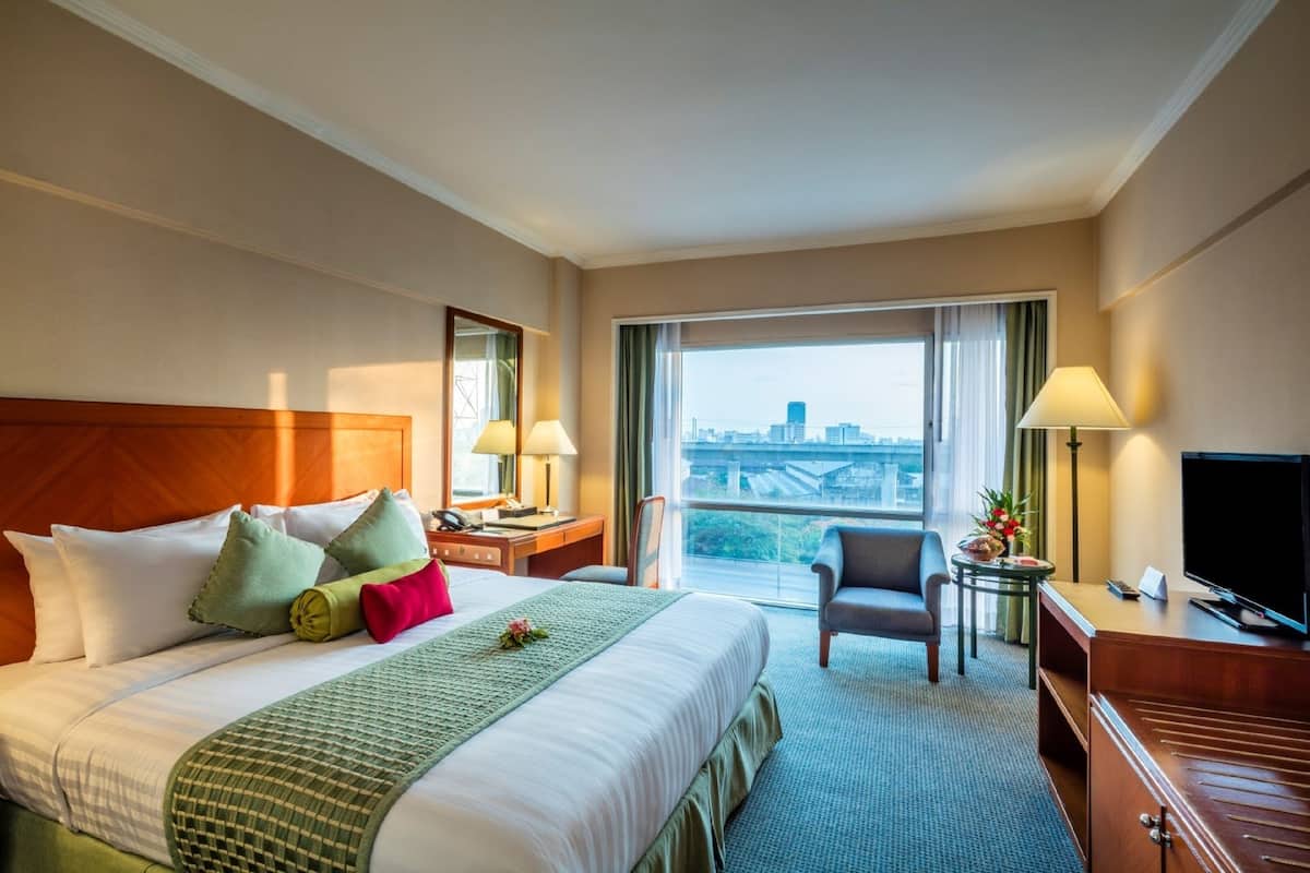 A hotel room with a large bed, a desk, a chair, a TV, and a view of a cityscape.