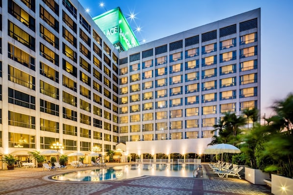 A hotel with a large pool area, multiple floors, and a prominent green sign on the building.