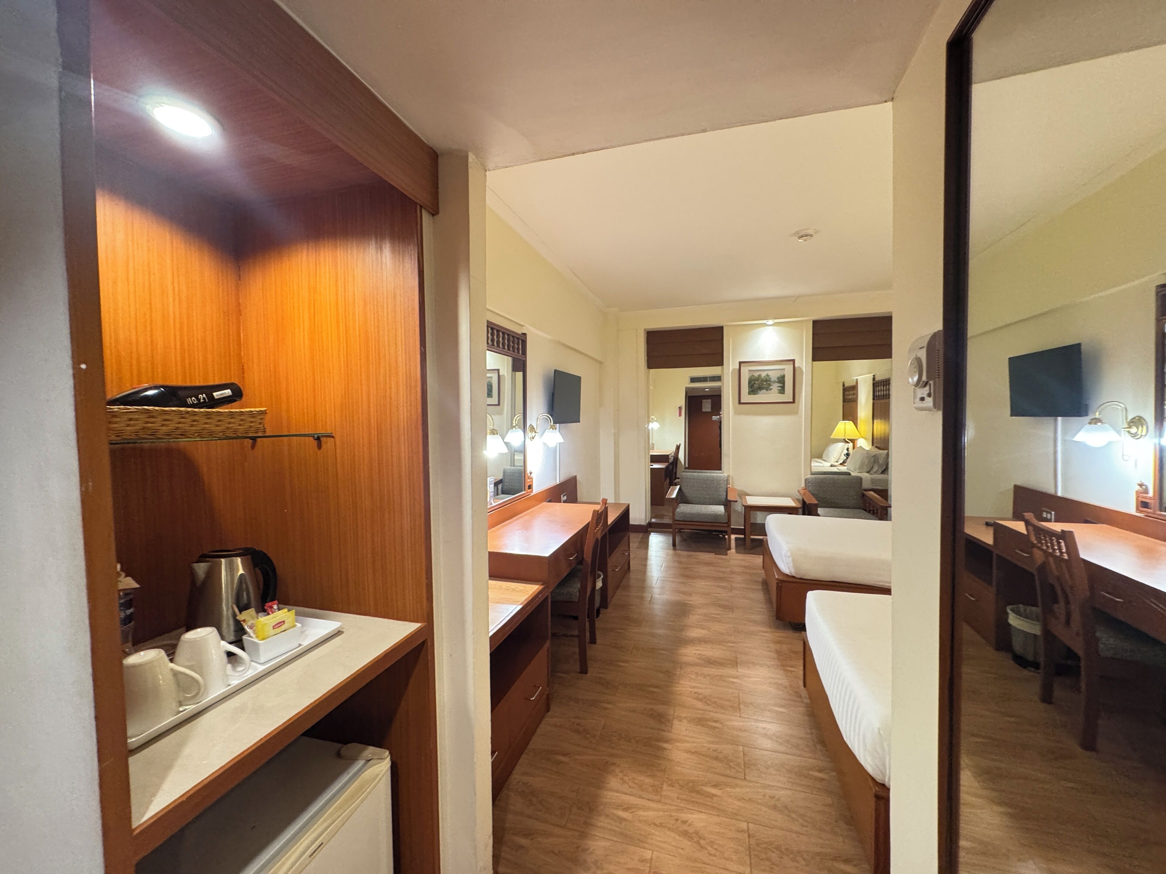 A hotel room with a wooden floor, a bed, a desk, a chair, a small table, and a mirror.