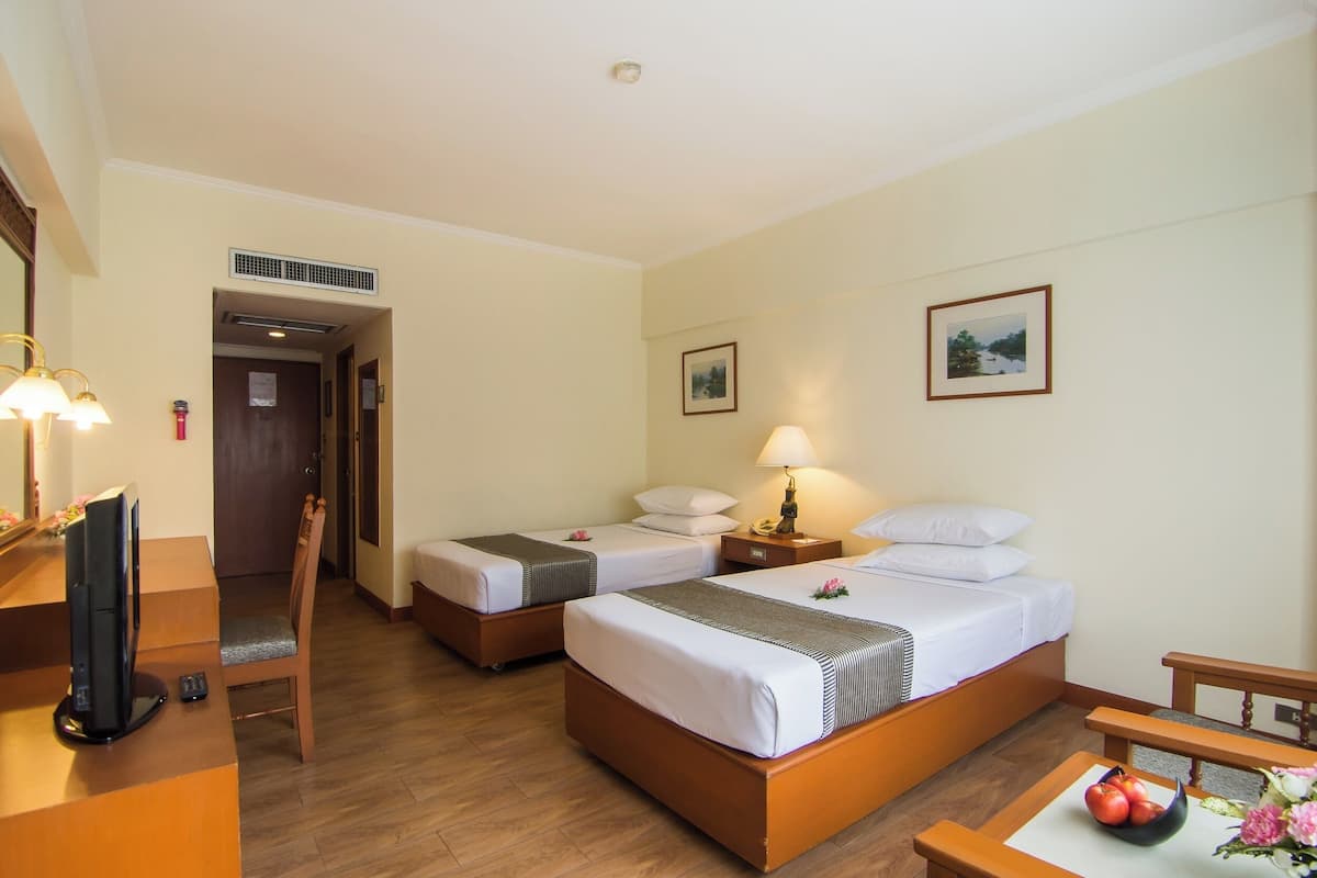A hotel room with two single beds, a desk with a television, a chair, and a small table with fruit.