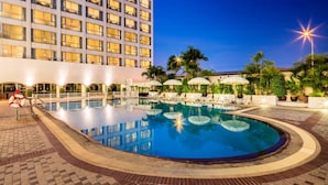 A swimming pool with lounge chairs and umbrellas, surrounded by palm trees and a hotel building in the background. - Bangkok Palace Hotel (Bangkok)
