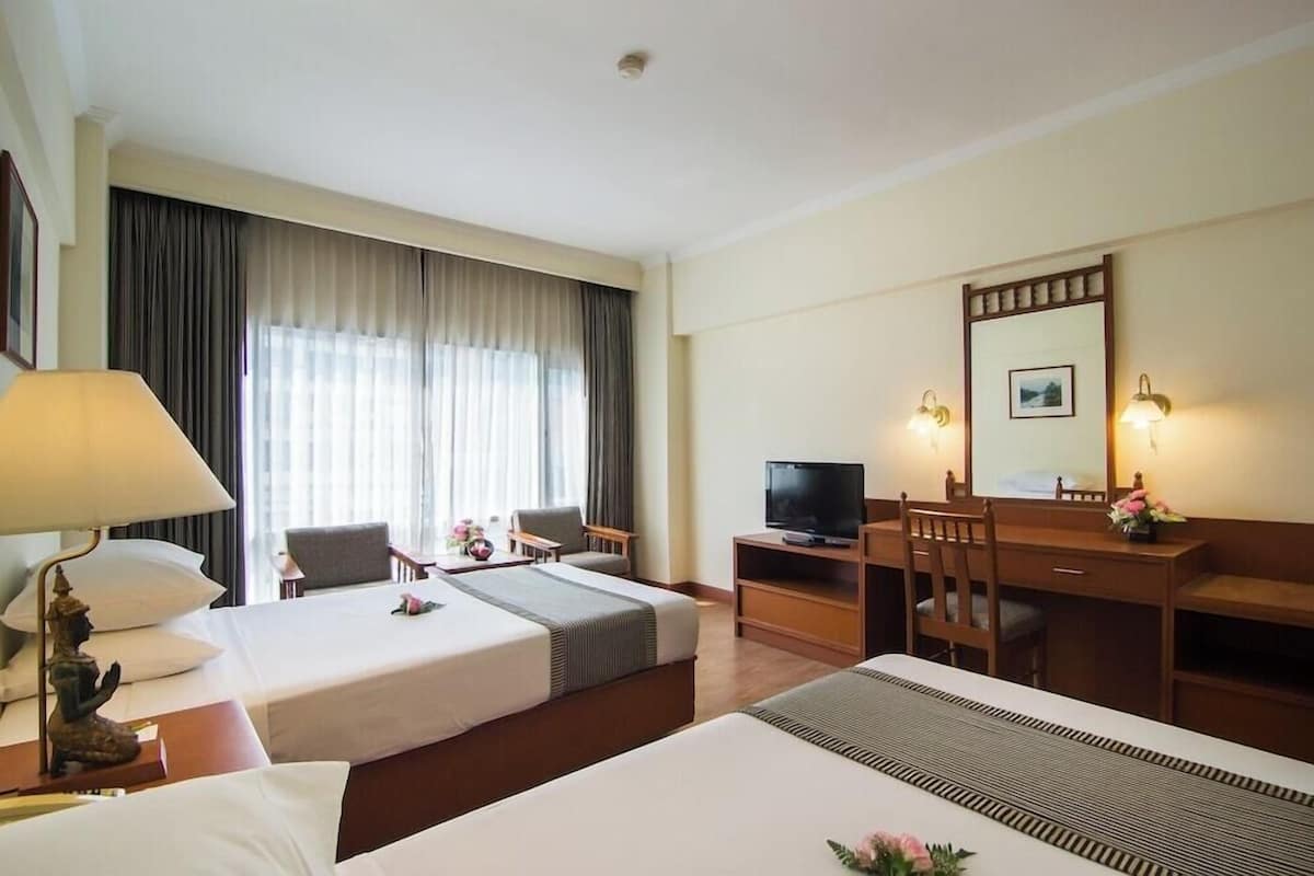 A hotel room with two beds, a desk, a television, and a large window with curtains.