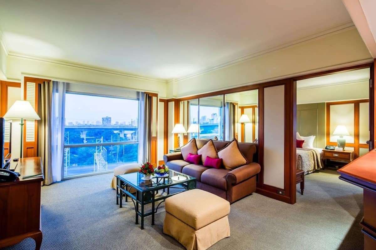 A hotel room with a large window, a sofa, a coffee table, and a desk.