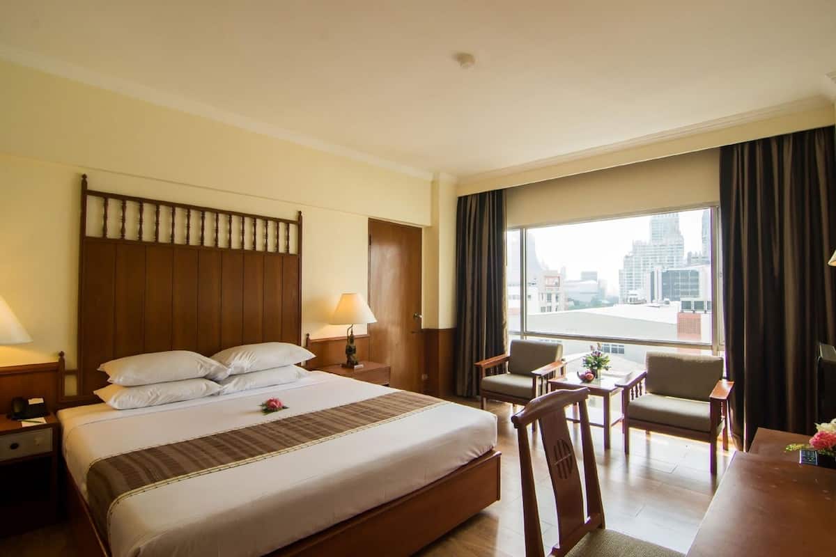 A hotel room with a large bed, two bedside tables, a desk with chairs, a view of the city, and a window with curtains.