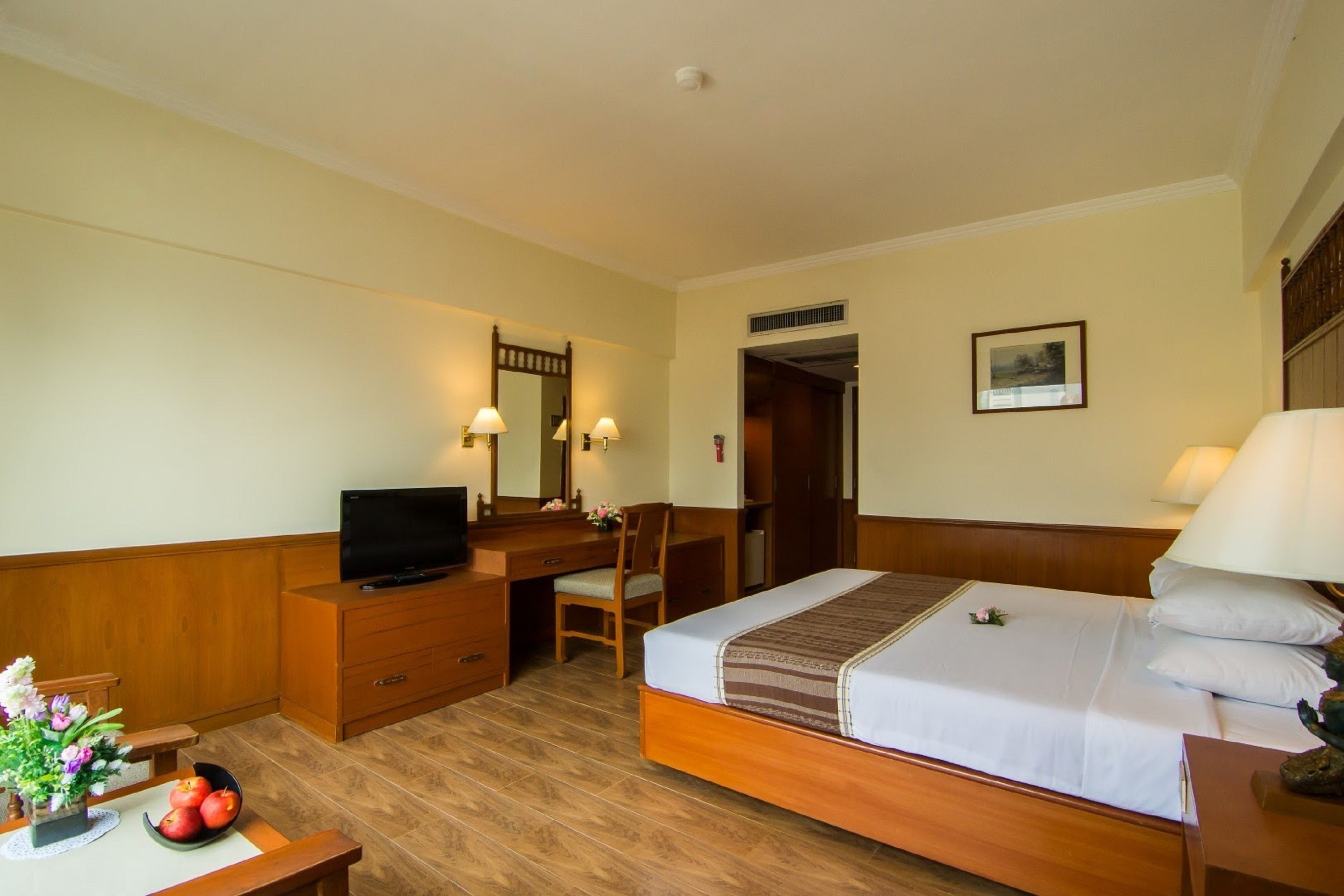 A hotel room with a bed, desk, chair, television, and a small table with flowers.