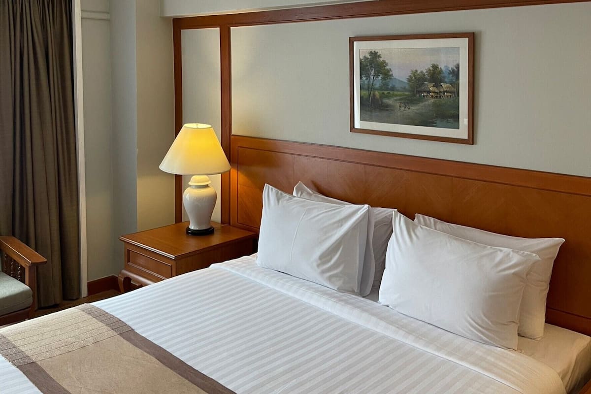 A hotel room with a large bed, a nightstand with a lamp, a framed picture on the wall, and a window with curtains.
