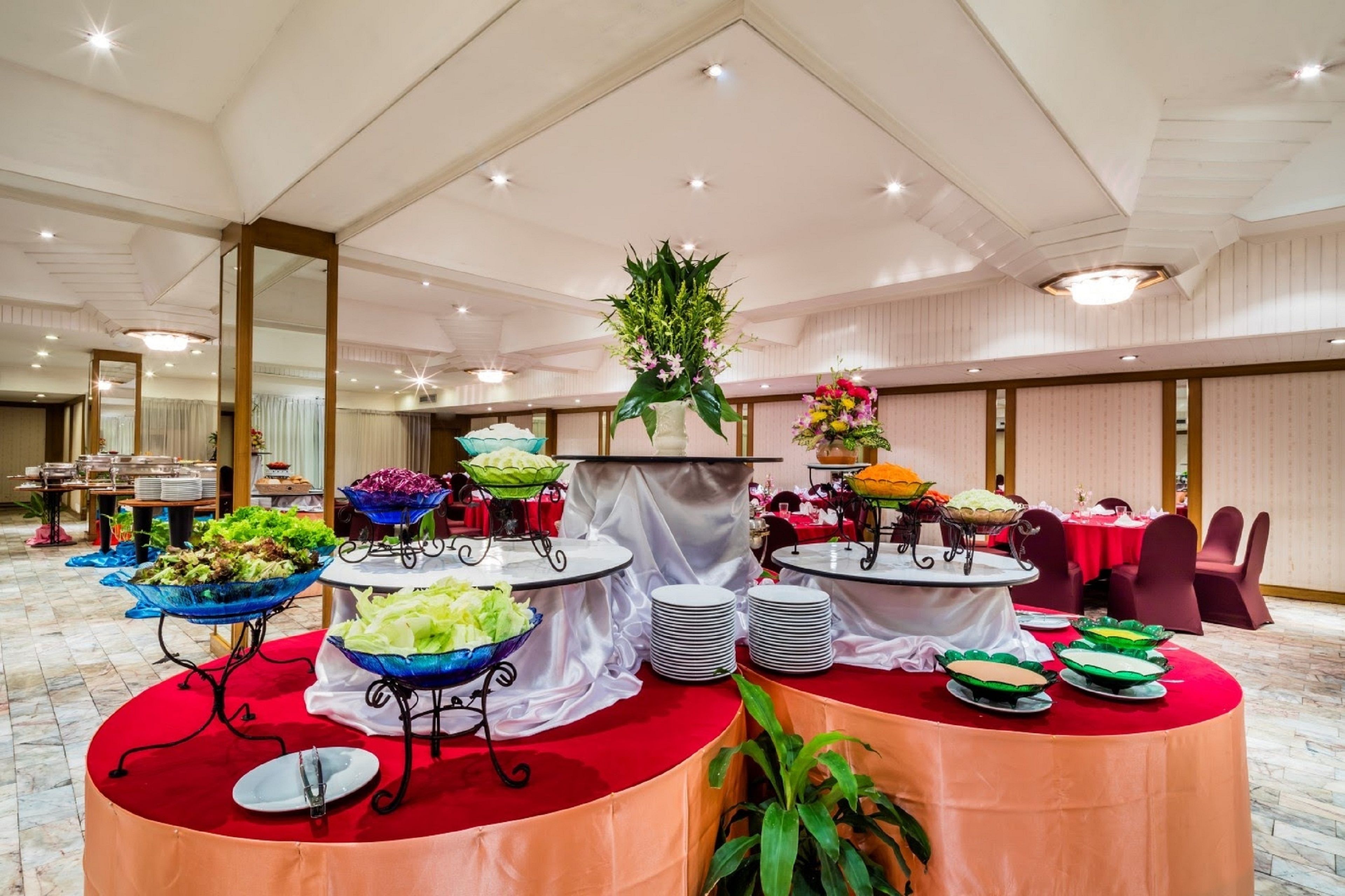 A buffet setup with various food stations, including salads and fruits, in a spacious room with high ceilings and a polished floor.