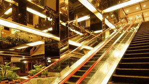 An indoor escalator with a modern design, surrounded by glass walls and illuminated by overhead lights. - Bangkok Palace Hotel (Bangkok)