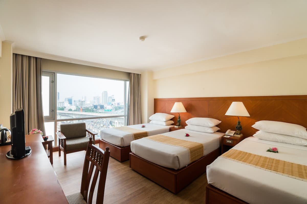 A hotel room with two beds, a desk, a chair, and a TV.
