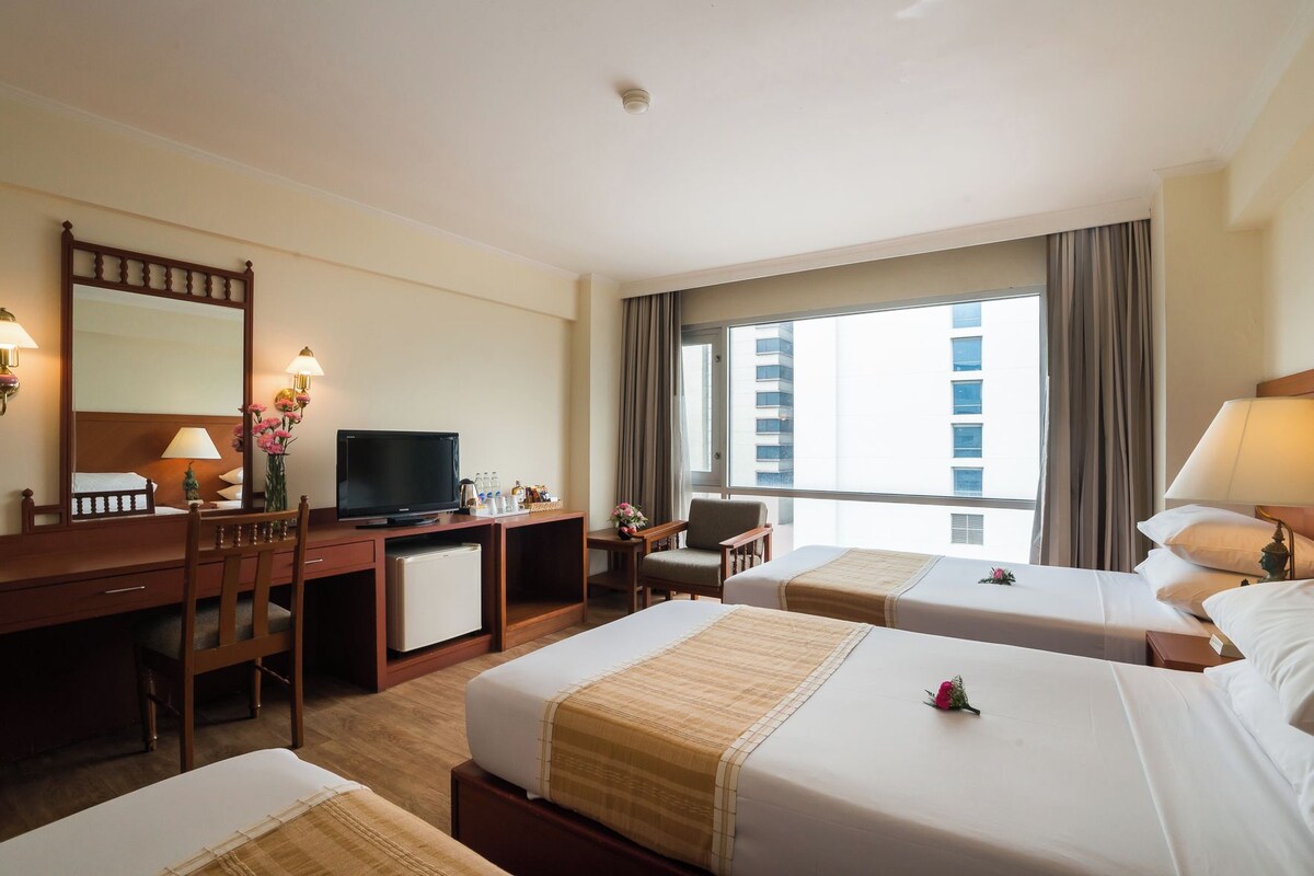 A hotel room with two beds, a desk, a television, and a large window with curtains.