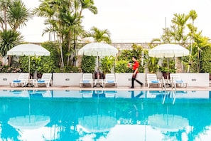 Una piscina al aire libre, sombrillas, sillones reclinables de piscina