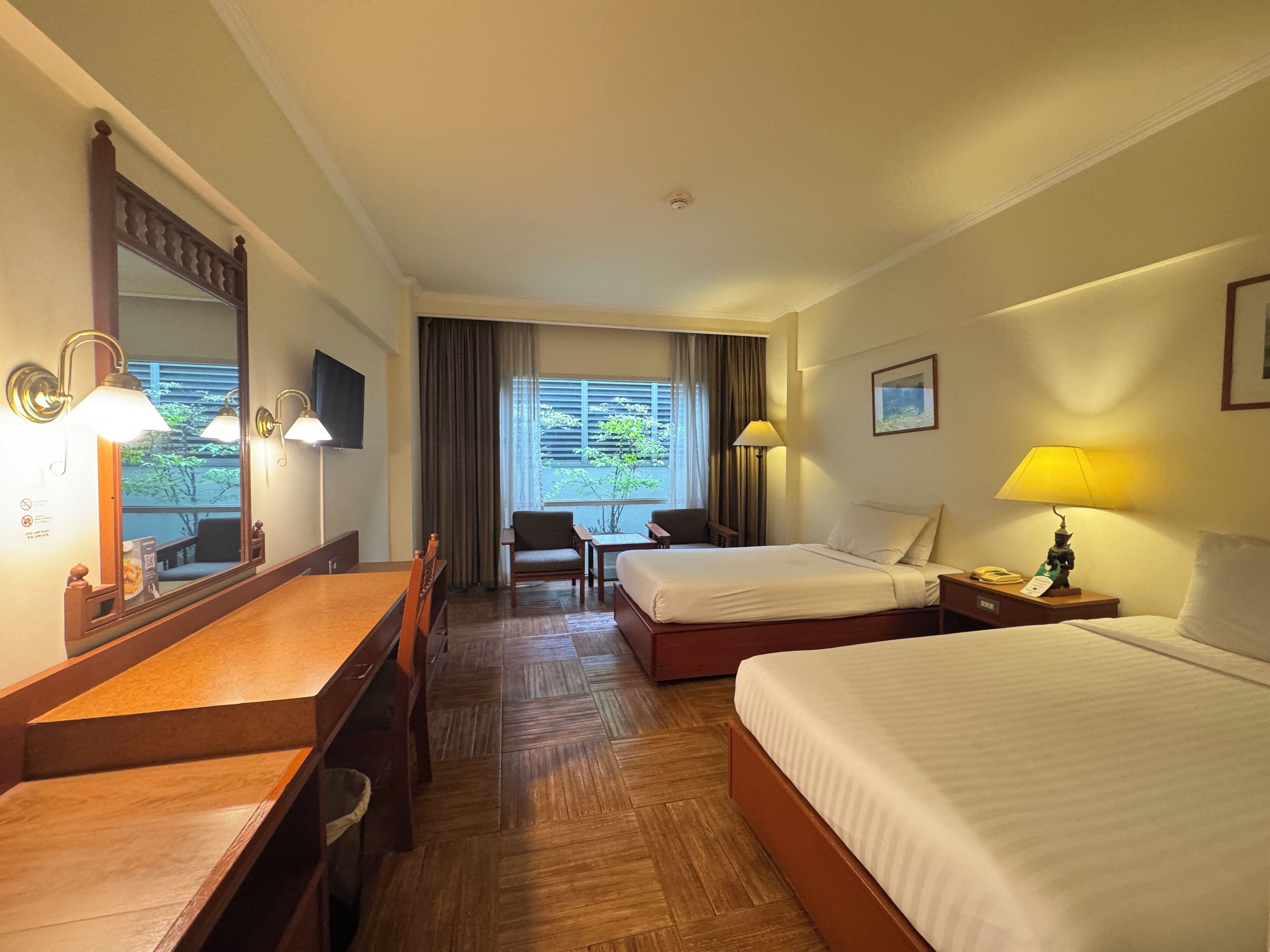 Une chambre d’hôtel avec un plancher en bois, un bureau avec une chaise, deux lits simples, une télévision et une fenêtre avec des rideaux.
