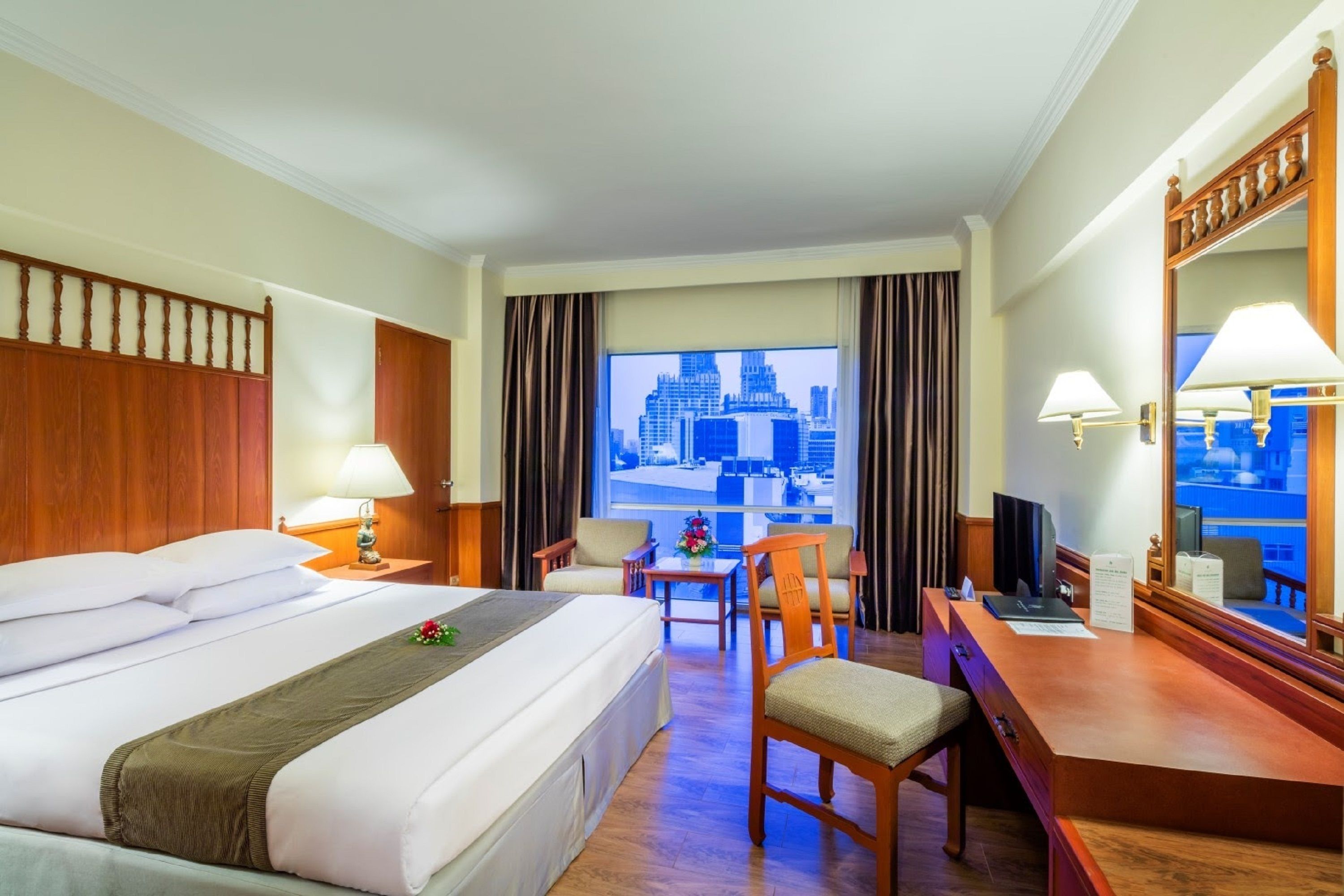 A hotel room with a large bed, a desk, a chair, a TV, and a window with a city view.