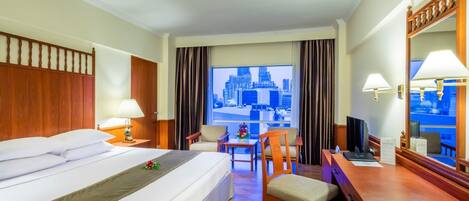 A hotel room with a large bed, a desk, a chair, a TV, and a window with a city view.