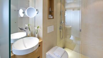 A modern bathroom with a large white sink, a glass-enclosed shower, and a toilet with a towel on top.