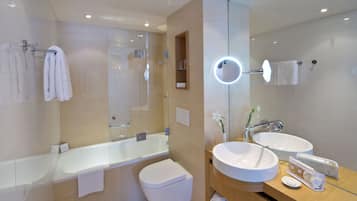 Un baño moderno con ducha envuelta en vidrio, una bañera blanca, inodoro y tocador con dos lavamanos y un espejo.