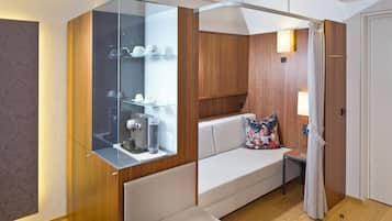 Une salle de bain moderne dotée d’une douche à parois de verre, d’un meuble-lavabo en bois et d’un coin salon avec un banc rembourré et une petite table.