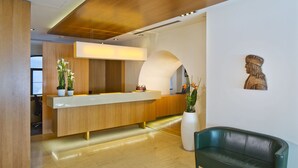 Un espace d’accueil moderne avec un comptoir de réception en bois, un canapé vert et un grand vase orné de plantes.
