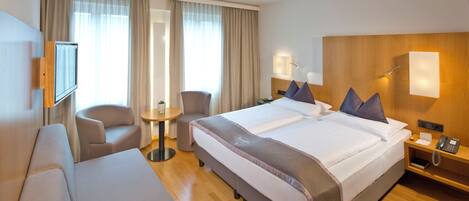 Hotelkamer met een groot bed, een bank, een stoel, een bijzettafeltje en een nachtkastje met een lamp en telefoon.