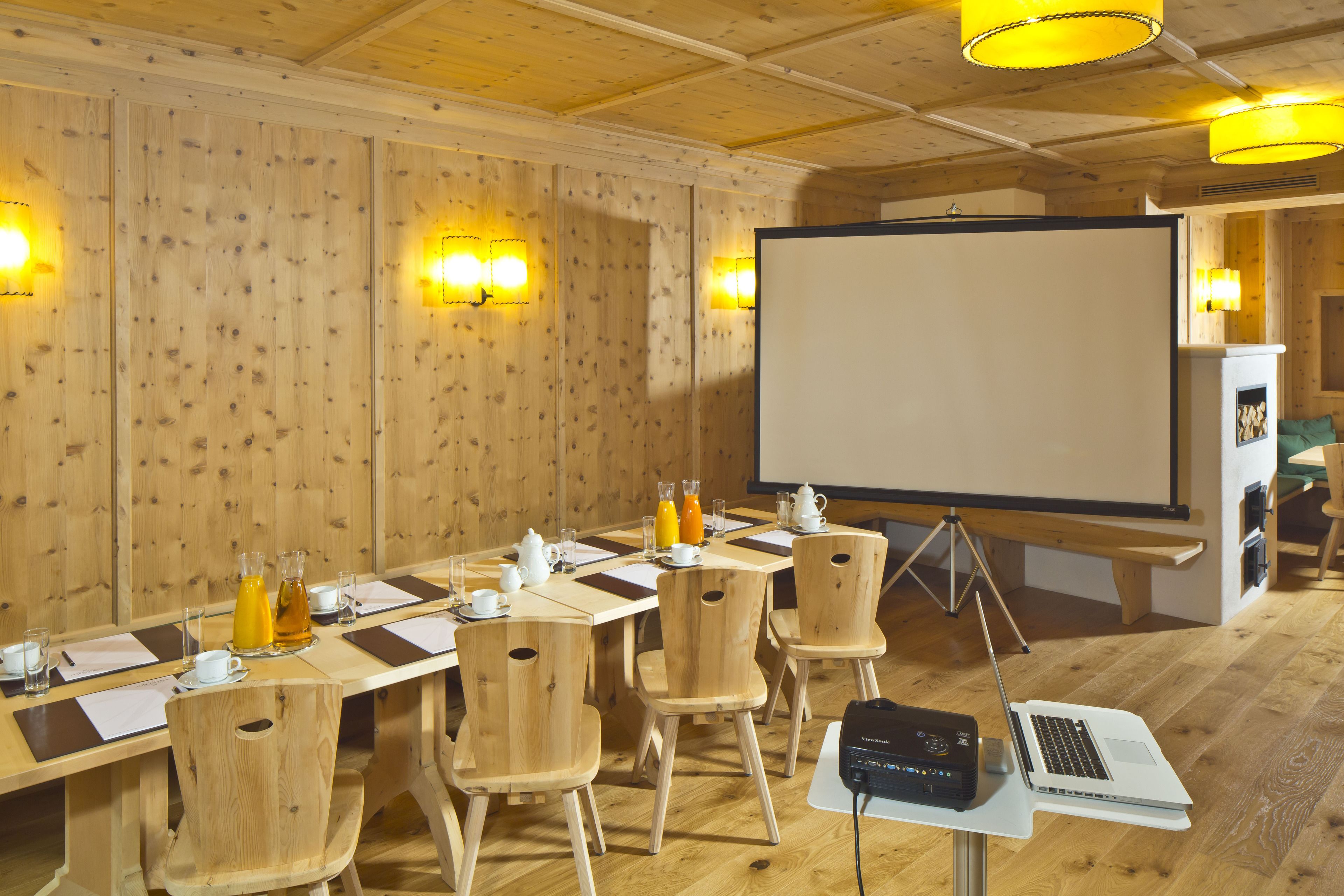 Una sala de conferències amb una taula llarga, cadires de fusta, una pantalla de projector i un ordinador portàtil sobre un suport.