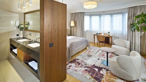 Une chambre d’hôtel avec un grand lit, un bureau, une chaise, un canapé et une salle de bain équipée d’un miroir et d’un lavabo.