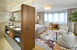 Een hotelkamer met een groot bed, een bureau, een stoel, een bank en een badkamer met spiegel en wastafel.