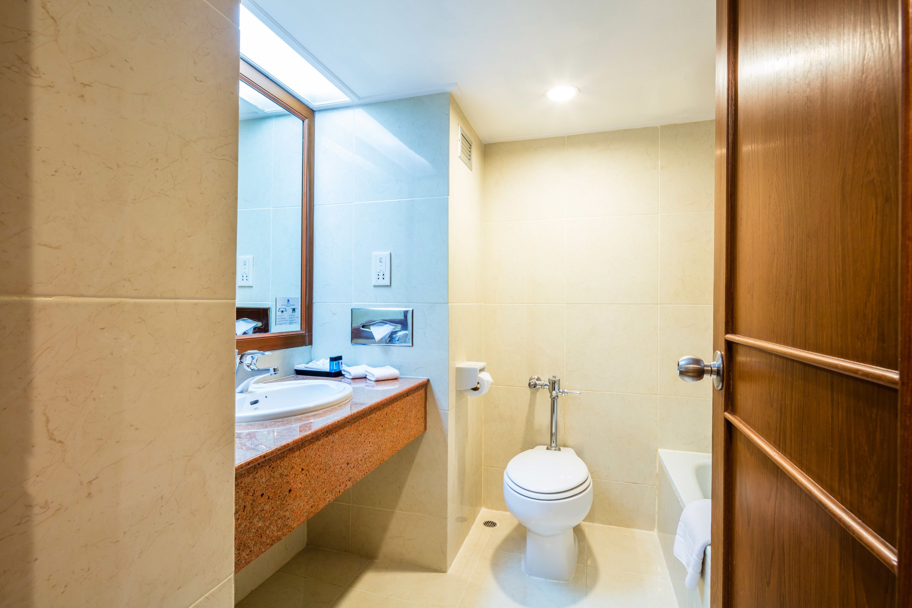 Un baño con lavamanos de mármol, inodoro y puerta de madera.