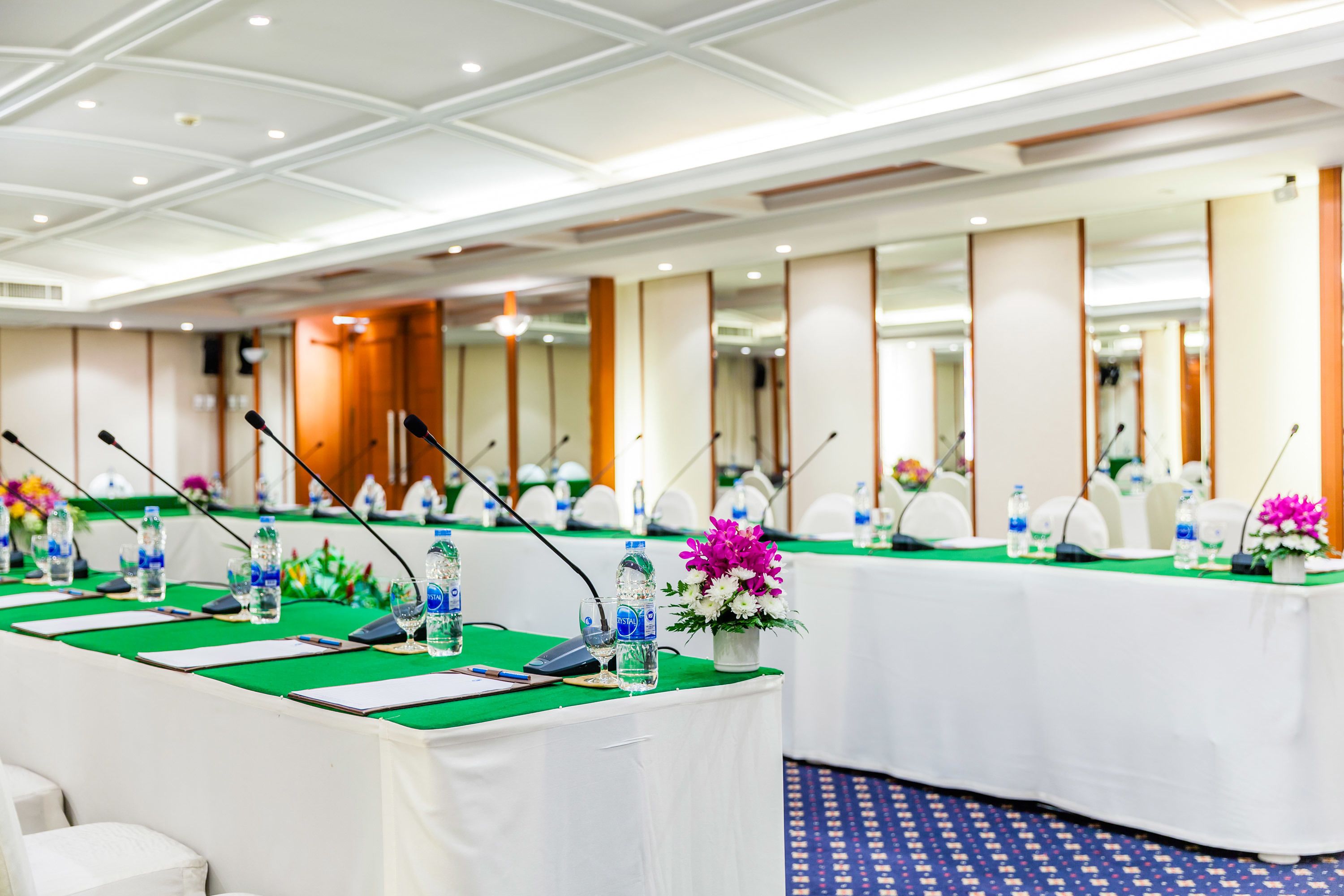 A conference room with tables set up for a meeting, equipped with microphones, water bottles, and floral centerpieces.