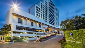 Un hotel moderno con un llamativo letrero que dice 'Chiclan Pattaya Resort', una entrada bien iluminada y un camino de entrada ajardinado.