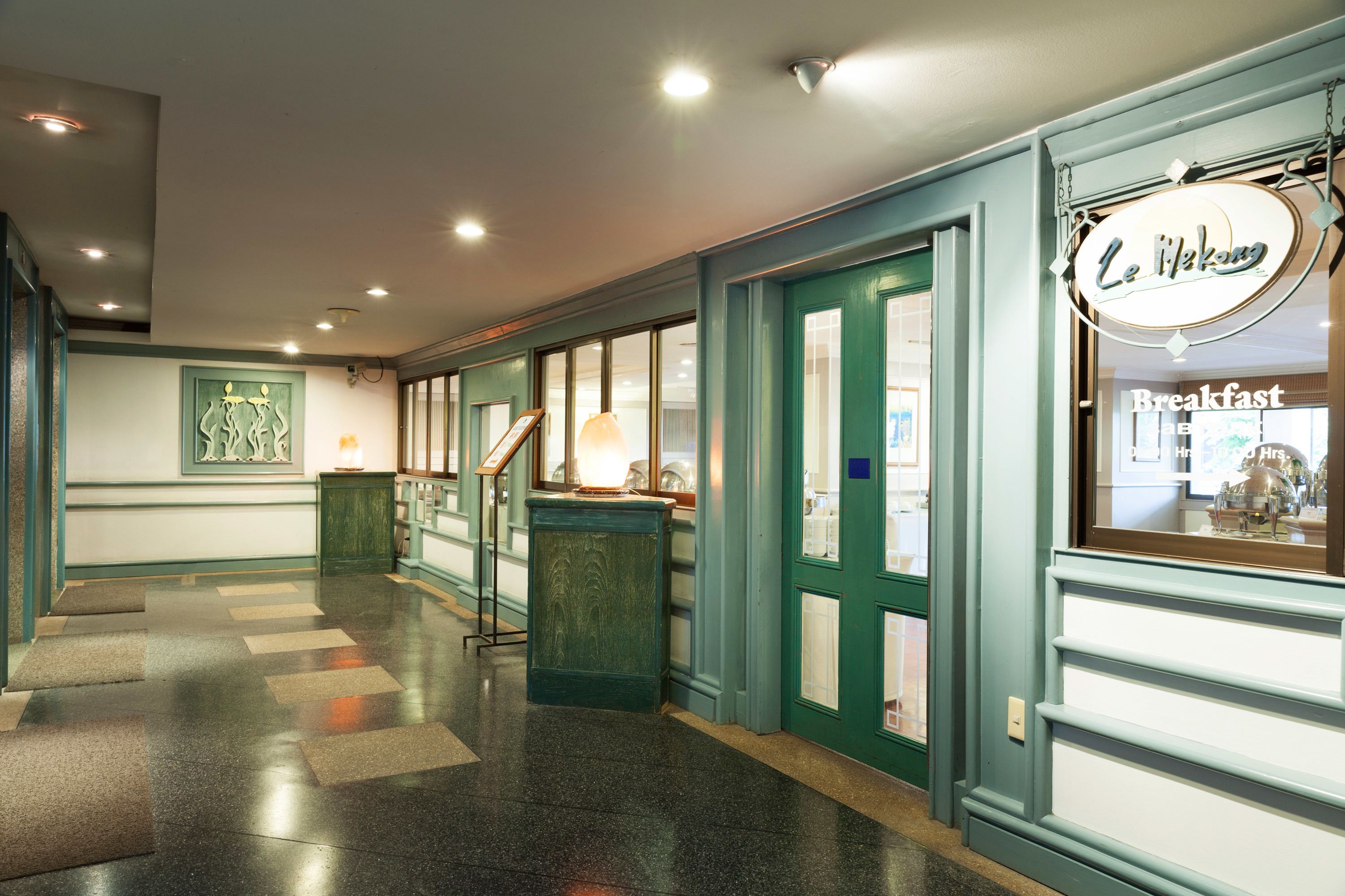 A hotel corridor with teal walls, a breakfast sign, and a framed artwork on the left.